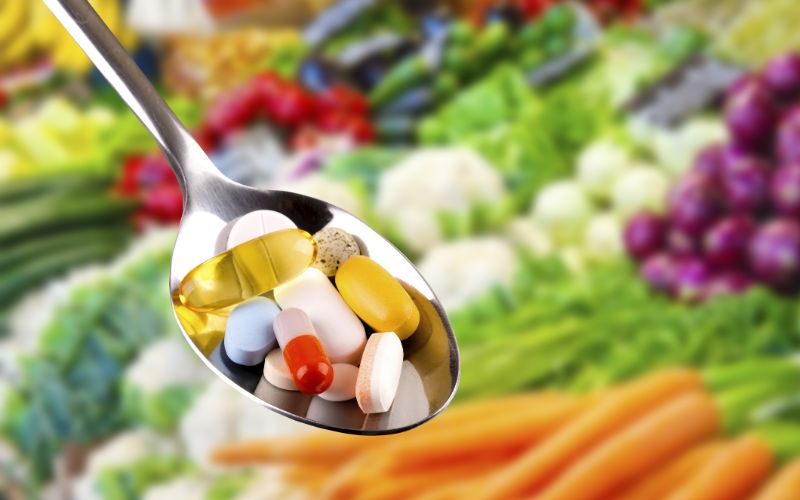 Vitamin-supplements-spoon-with-pills-dietary-supplements-on-vegetables-background-65371234-min-min