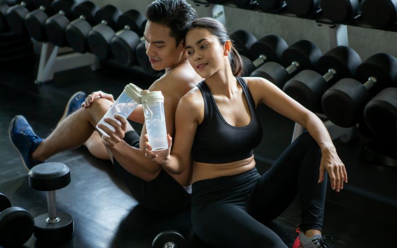 powder-for-gym-sport-man-and-woman-sitting-on-floor-tired-taking-a-break-drinking-water-after-exercise-workout-asian-couple-fitness-min