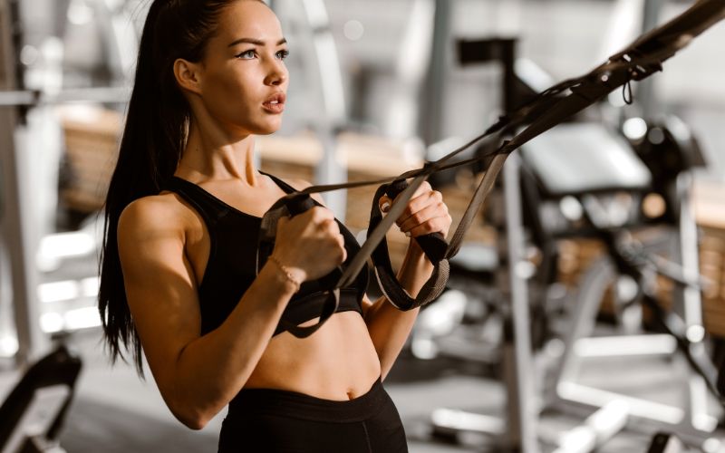 protein-supplements-athletic-dark-haired-girl-dressed-in-black-sports-top-and-shorts-is-working-out-on-the-fitness-station-in-the-gym-min