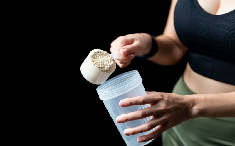 npl-supplements-close-up-of-women-with-measuring-scoop-of-whey-protein-and-shaker-bottle-preparing-protein-shake-min